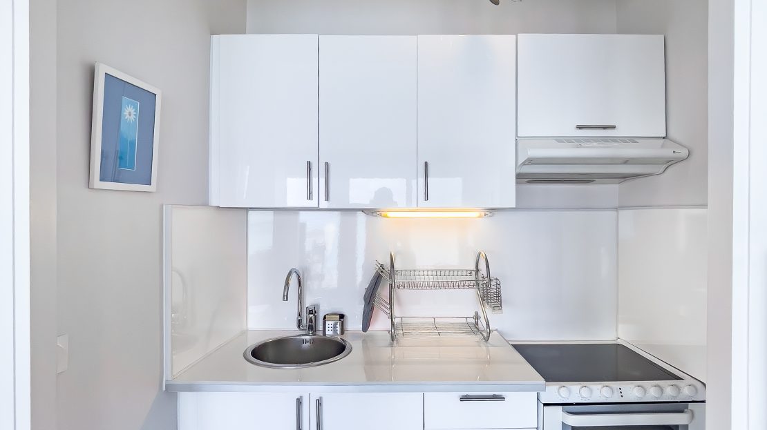 Cuisine blanche compacte avec évier, four et hotte de cuisine